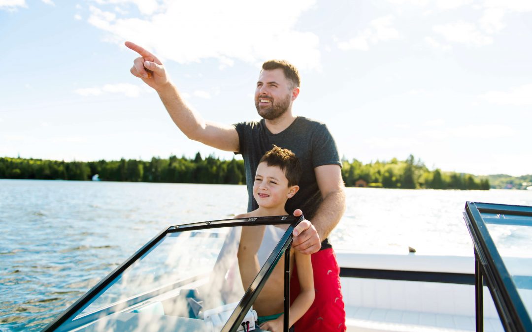 Dad driving boat with son wearing a lifejacket